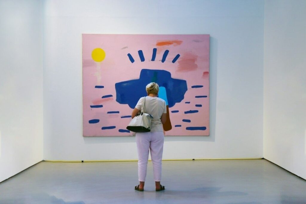 Gallery visitor studying a colorful abstract painting on a pink canvas